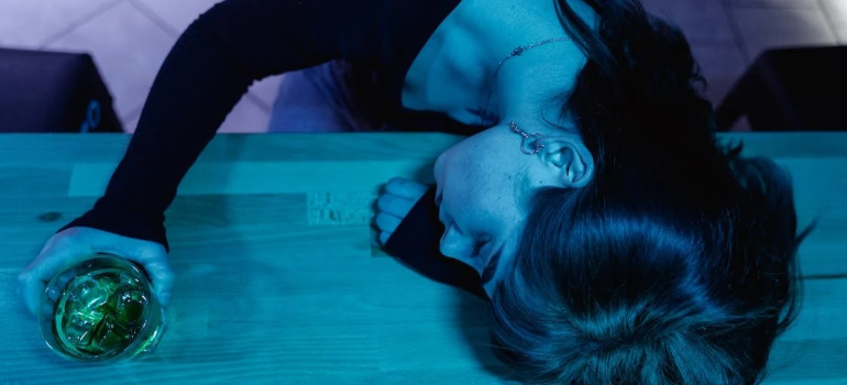 A woman passed out on a bar counter with a drink in hand showing how alcohol affects sleep.