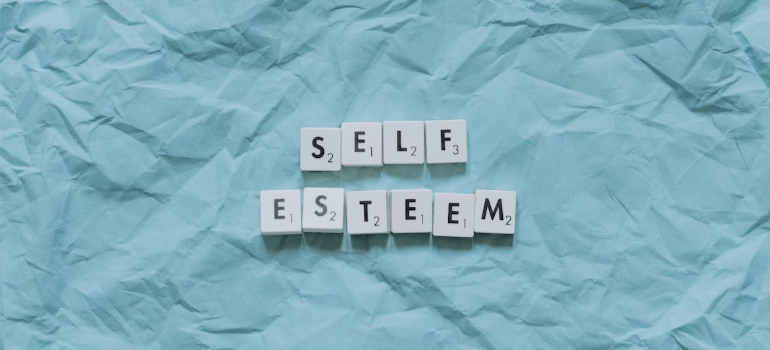 Letter tiles that spell out “self-esteem” on a blue background.