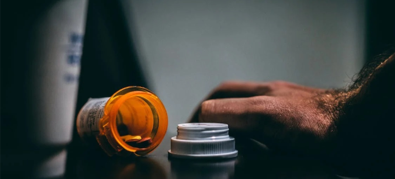 A close-up of a man’s hand next to a bottle of pills for a post about addiction relapse triggers.
