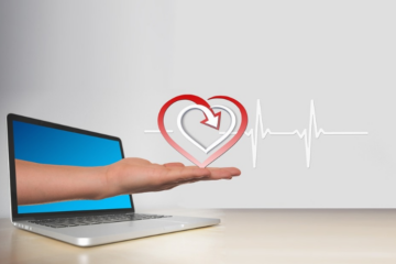 An illustration of a hand holding a heart emerging from a laptop, illustrating the debate of telehealth vs in-person rehab.