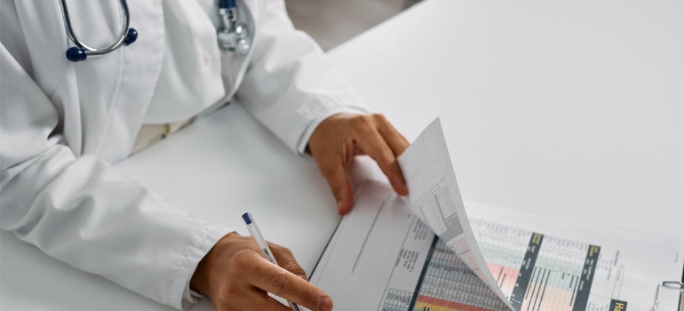 A close-up of a doctor looking through papers on a desk.