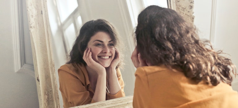 A woman looking at the mirror and smiling representing the positive self-image needed to reclaim your life after an addiction