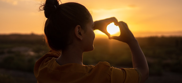 a woman forming a heart with hands at sunset