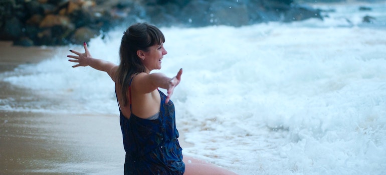 woman in bathing suit sitting on shore embracing waves with a smile depicts how crucial mental health during addiction recovery is 