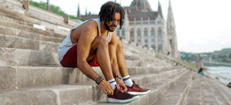 A close-up of a young man tying his shoelaces on stairs, illustrating the connection between physical health and recovery capital.