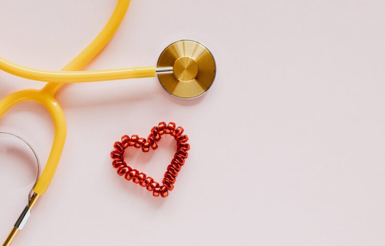 A yellow stethoscope next to a red heart on a pink surface representing starting your rehab program in Texas